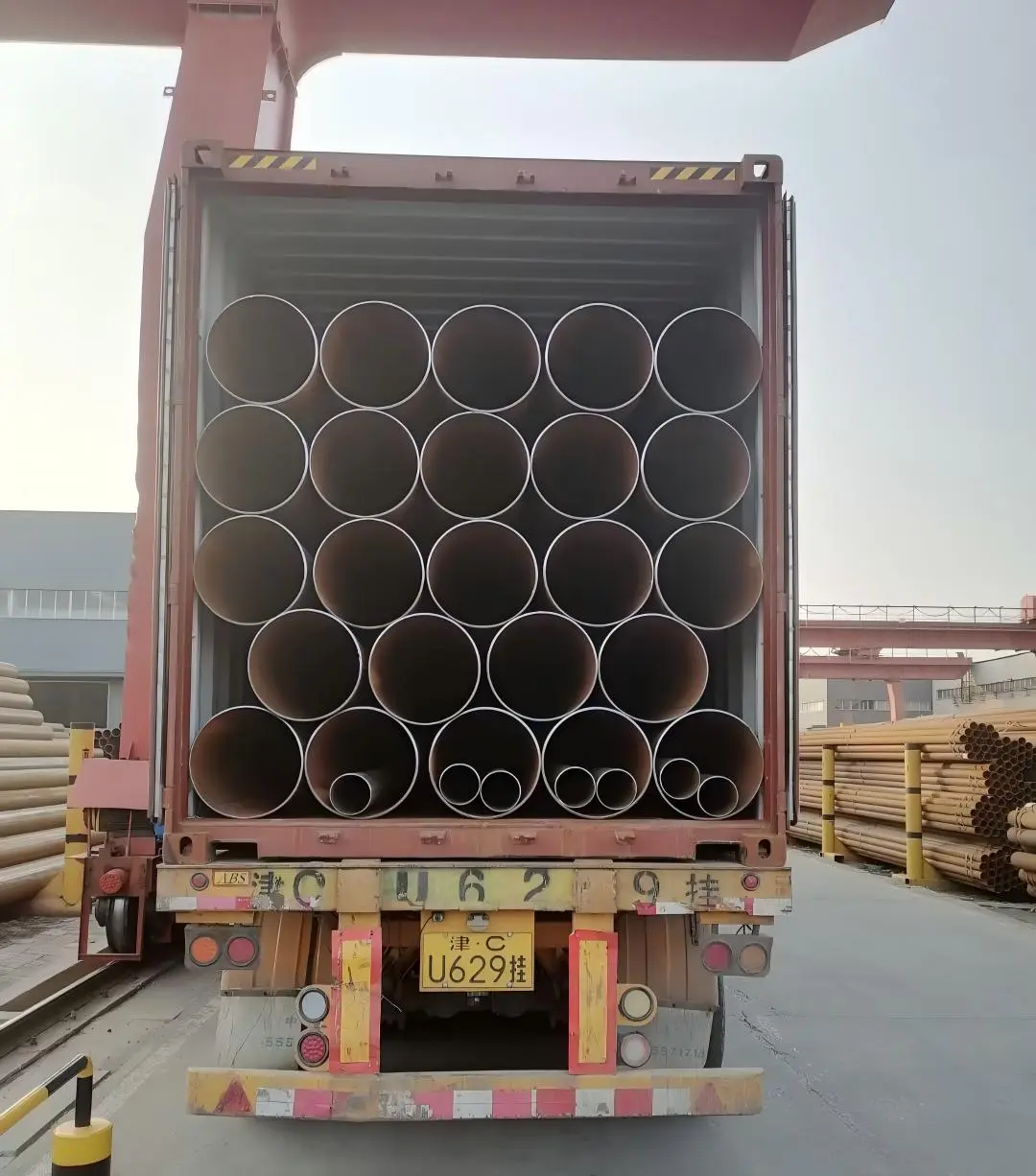 Crane loading strapped steel tube bundles onto a truck for container delivery